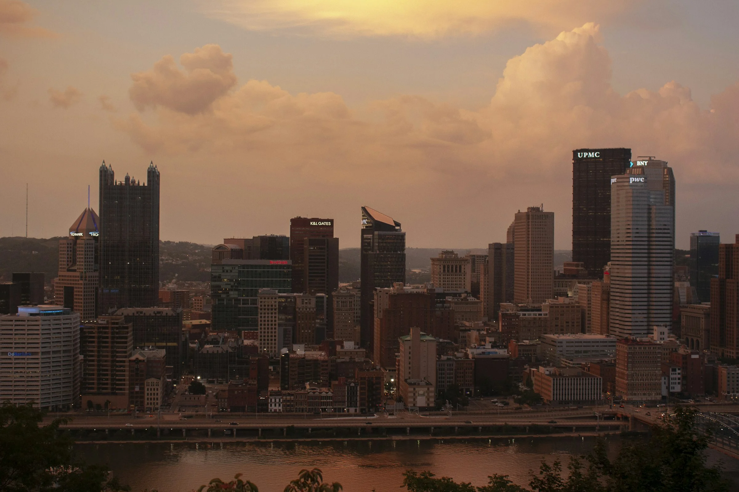 The Pittsburgh skyline at golden hour with clouds above the river